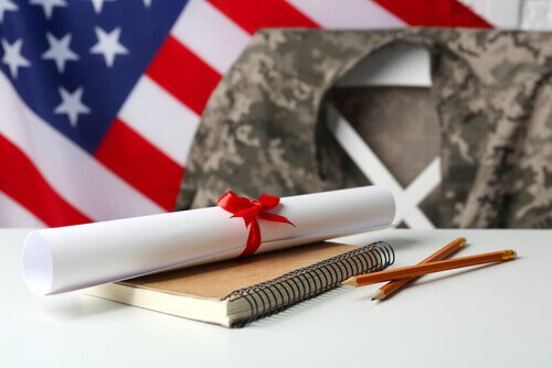 pencils, book, and diploma laying on table with military uniform and U.S flag in background