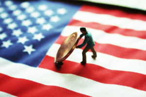 Small figure of military service member carrying a coin/debt on top of U.S flag