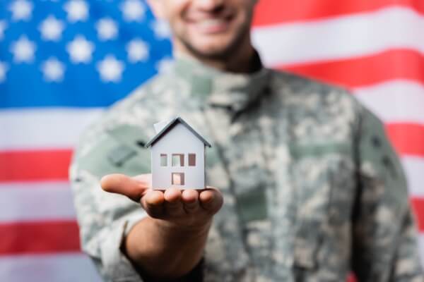 House model in hand of happy military man in uniform near american flag on blurred background.