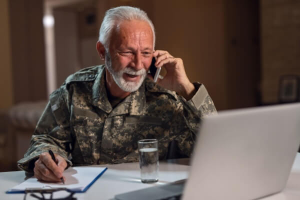 Smiling senior sergeant communicating on mobile phone while doing paperwork and using laptop in the office.